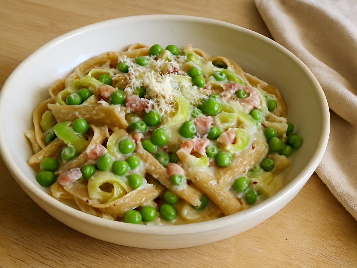 Romige pasta met spekjes, prei en doperwten in een schaal